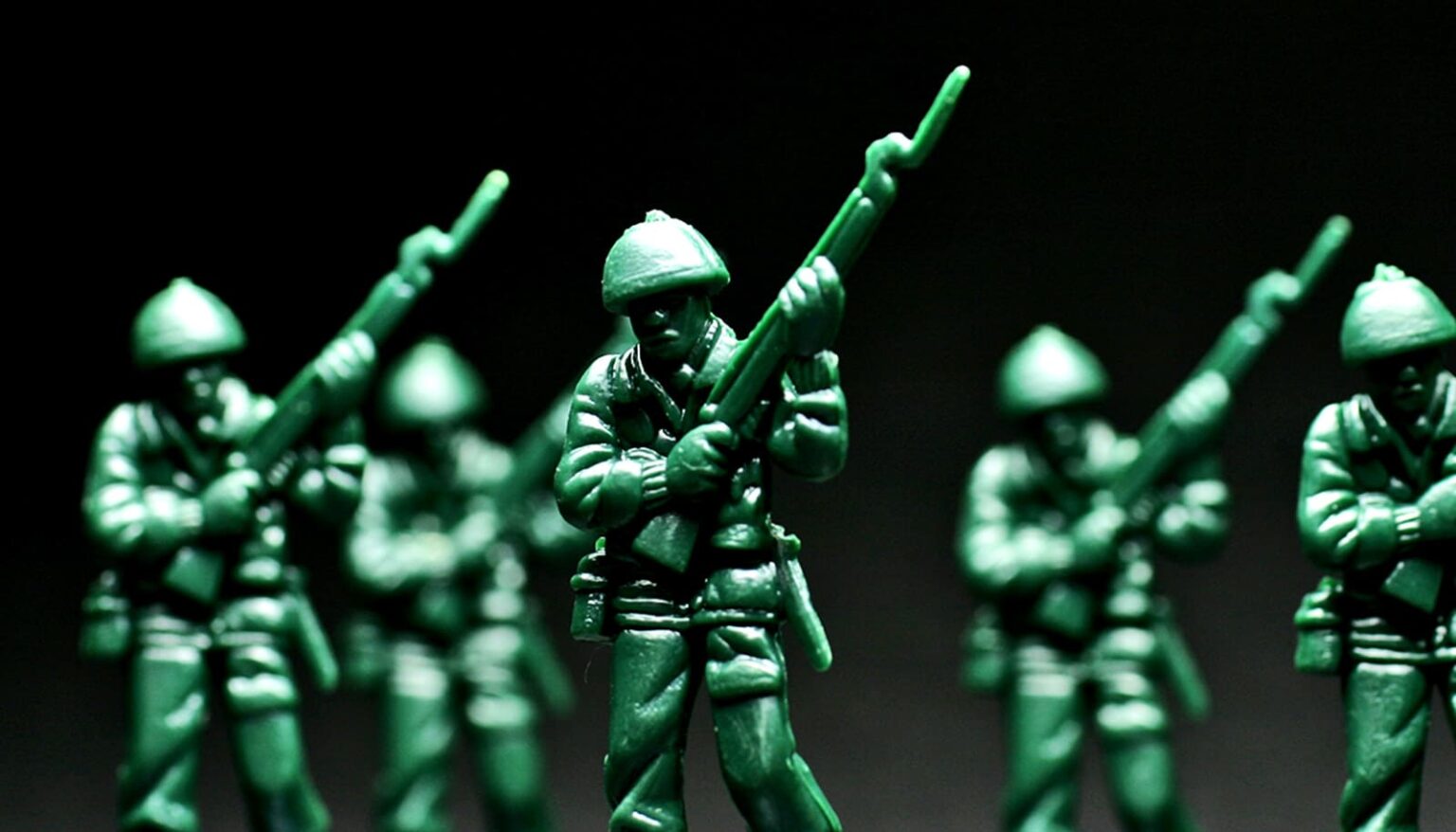 A row of green toy soldiers against a dark background.